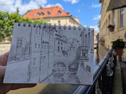 A pencil sketch of the Čertovka canal in Prague, with the real view in the background