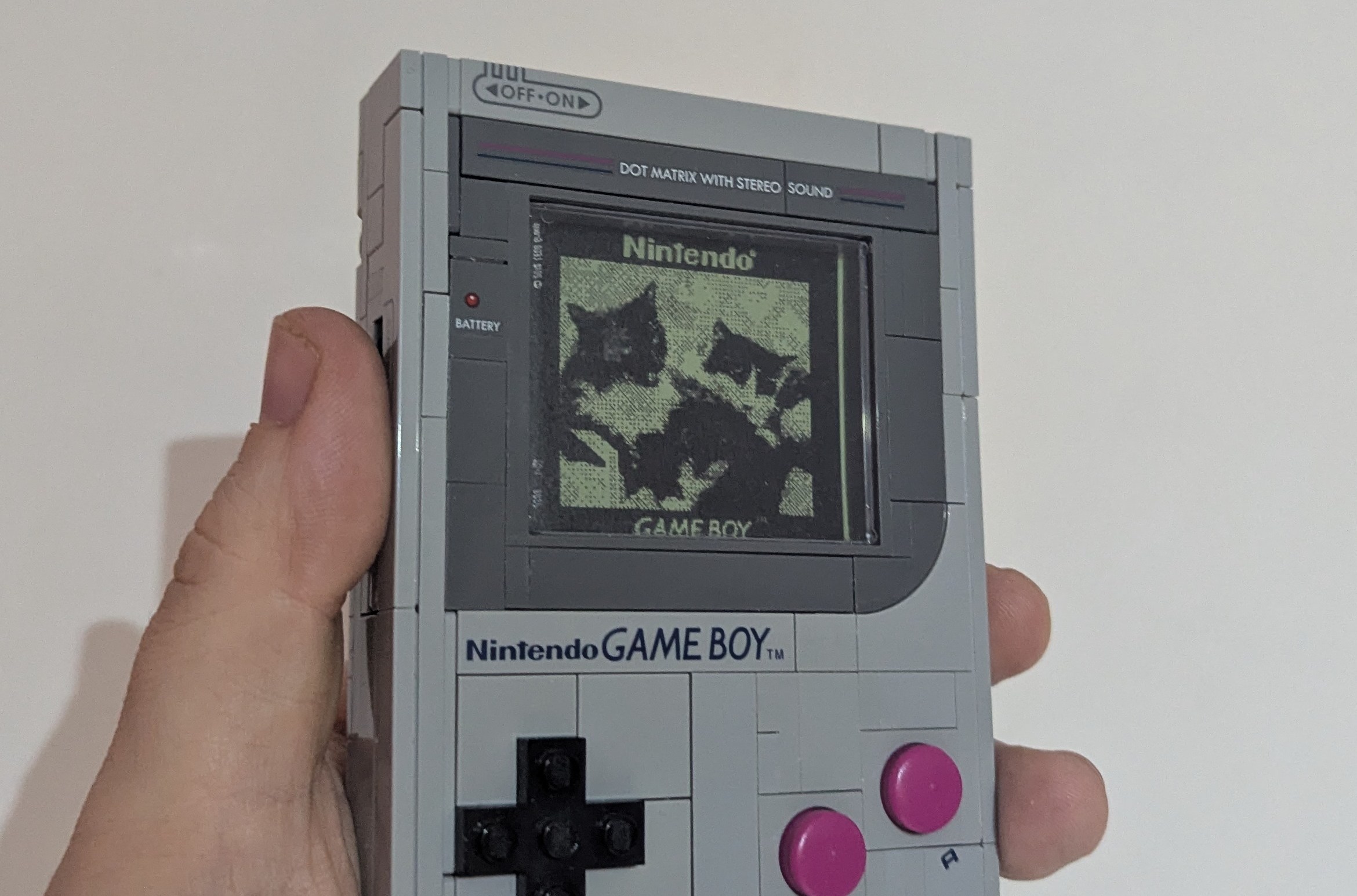 A Lego Game Boy, whose screen is showing a photo of two cats. The photo has been treated to look like a Game Boy Camera photo (although there is no Lego Game Boy Camera in the cartridge slot so who knows how that's supposed to be happening)